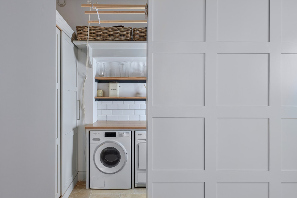 Mid-sized transitional single-wall dedicated laundry room in West Midlands with grey cabinets, wood benchtops, white splashback, subway tile splashback, white walls, an integrated washer and dryer, beige floor and brown benchtop.