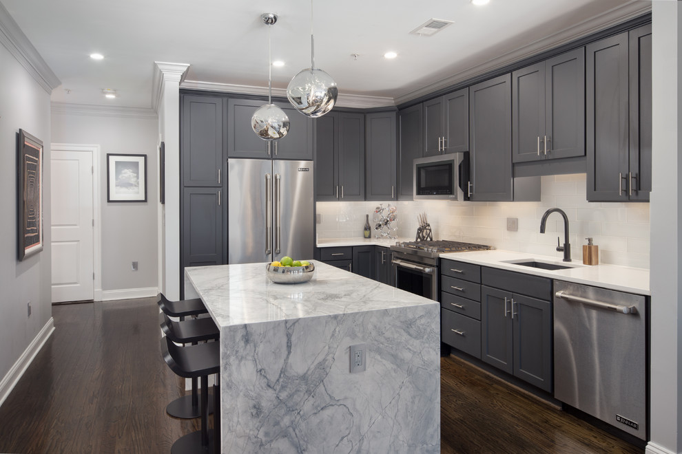 Inspiration for a transitional l-shaped kitchen in DC Metro with an undermount sink, shaker cabinets, grey cabinets, white splashback, stainless steel appliances, dark hardwood floors, with island, brown floor and white benchtop.