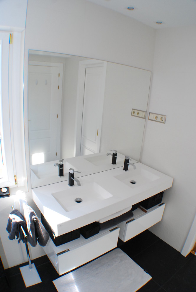 Diseño de cuarto de baño moderno con sanitario de pared, baldosas y/o azulejos blancas y negros, paredes blancas, lavabo suspendido y encimera de acrílico