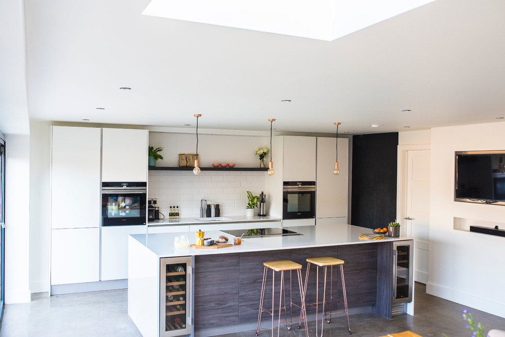 Design ideas for a large contemporary galley open plan kitchen in Other with a single-bowl sink, flat-panel cabinets, white cabinets, quartzite benchtops, white splashback, porcelain splashback, black appliances, concrete floors, with island, grey floor and white benchtop.