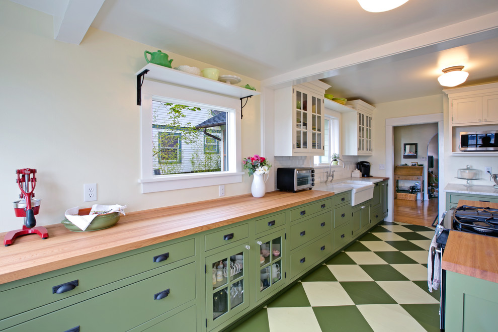Example of an arts and crafts u-shaped painted wood floor enclosed kitchen design in Seattle with a farmhouse sink, glass-front cabinets, green cabinets, wood countertops, white backsplash, subway tile backsplash, stainless steel appliances and an island