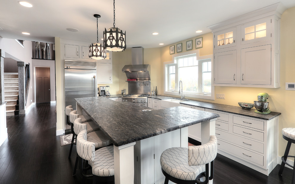 Inspiration for a mid-sized transitional l-shaped dark wood floor eat-in kitchen remodel with a farmhouse sink, shaker cabinets, white cabinets, metallic backsplash, stainless steel appliances, granite countertops and an island