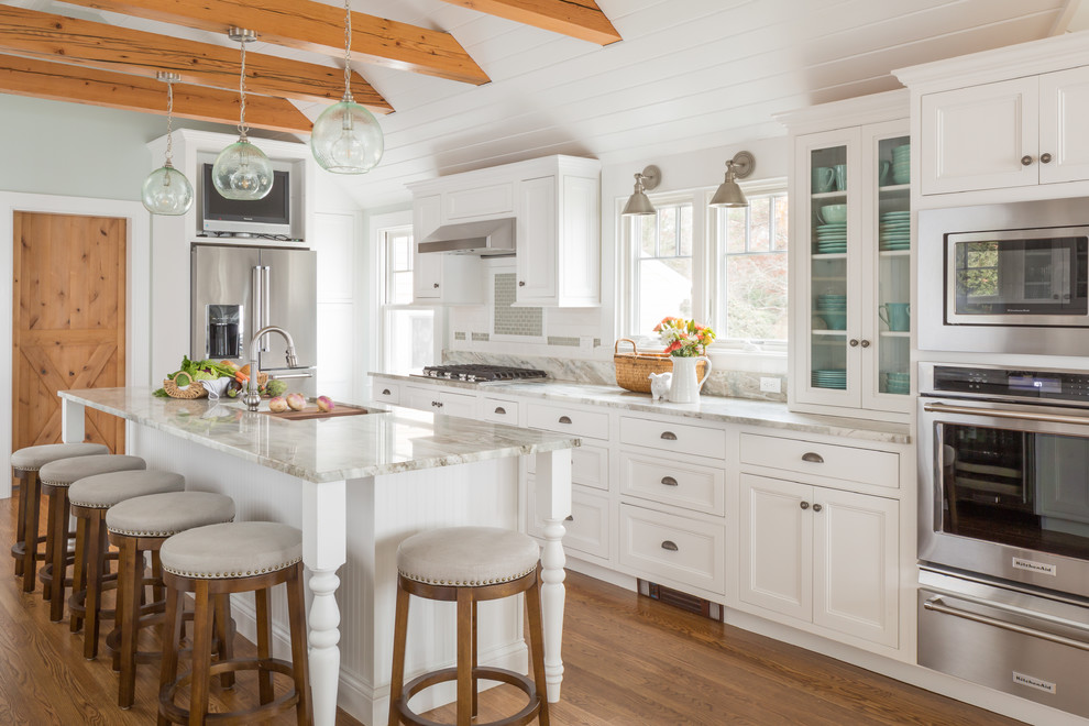 This is an example of a large beach style galley open plan kitchen in Boston with an undermount sink, recessed-panel cabinets, white cabinets, stainless steel appliances, medium hardwood floors, brown floor, subway tile splashback, quartzite benchtops, white splashback and with island.
