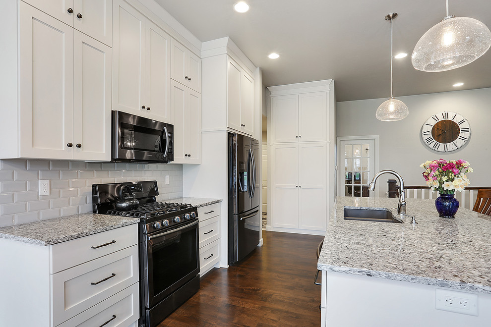 Open concept kitchen - mid-sized transitional medium tone wood floor and brown floor open concept kitchen idea with an undermount sink, flat-panel cabinets, white cabinets, granite countertops, ceramic backsplash, stainless steel appliances, an island and multicolored countertops