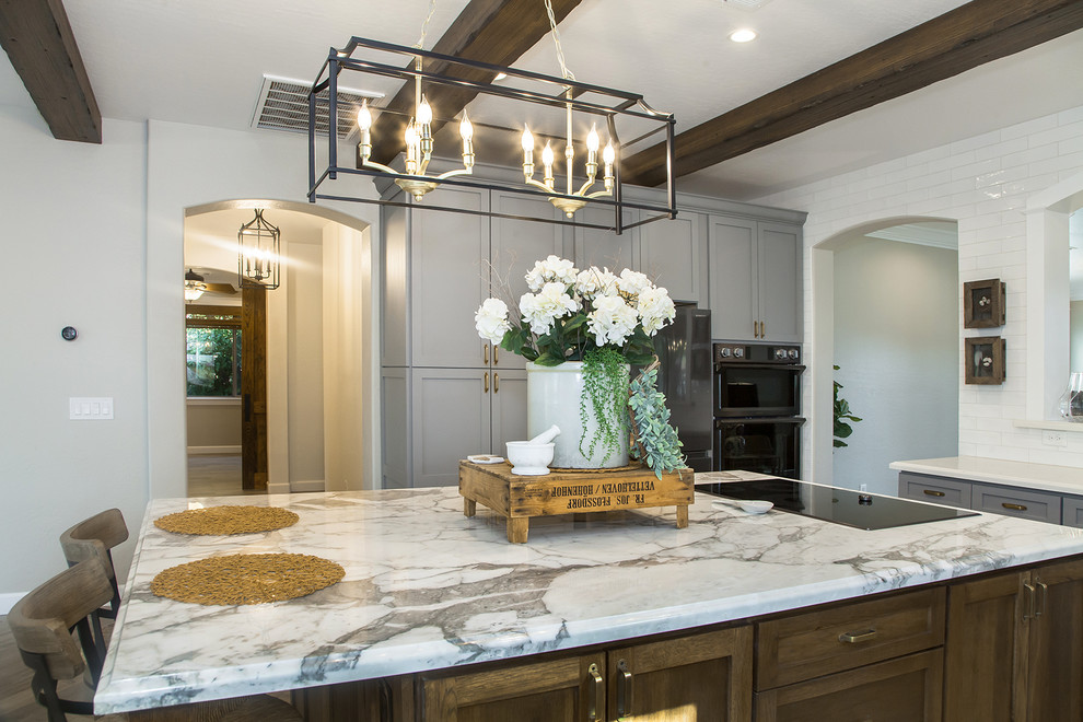 Large transitional l-shaped porcelain tile and brown floor eat-in kitchen photo in Phoenix with a farmhouse sink, shaker cabinets, gray cabinets, quartz countertops, white backsplash, glass sheet backsplash, stainless steel appliances, an island and white countertops