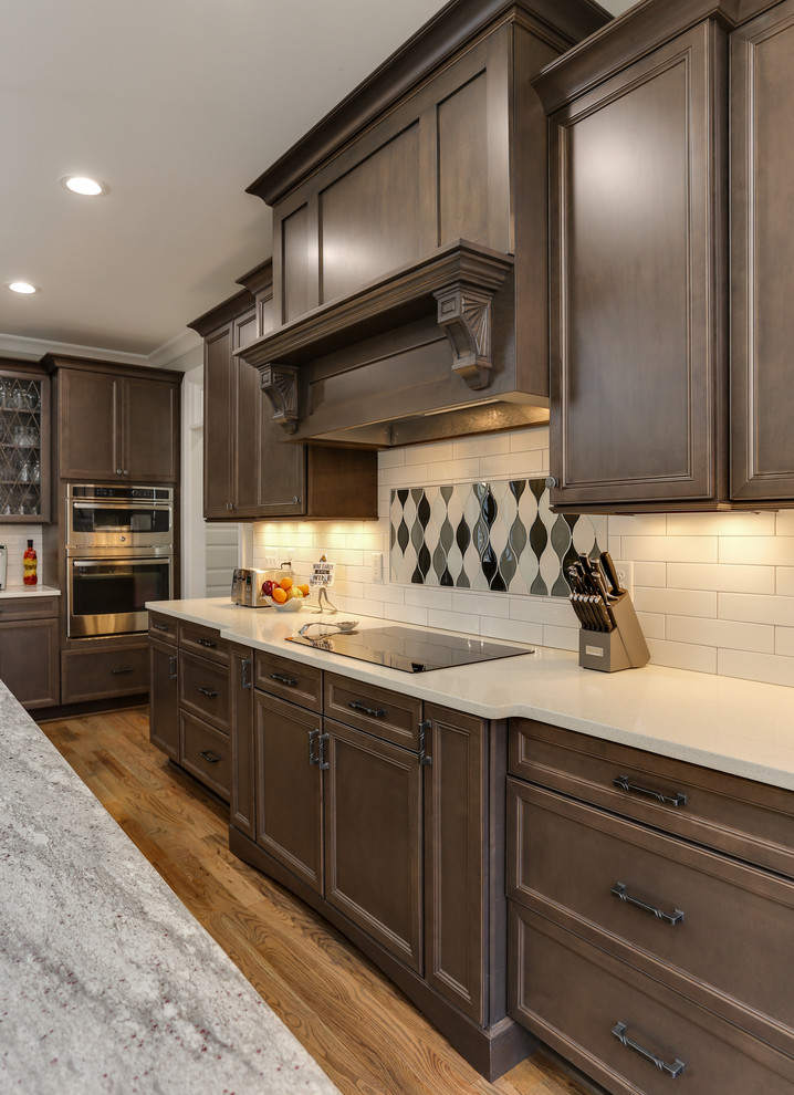Inspiration for a mid-sized transitional l-shaped open plan kitchen in Raleigh with an undermount sink, recessed-panel cabinets, grey cabinets, granite benchtops, white splashback, ceramic splashback, stainless steel appliances, medium hardwood floors and with island.