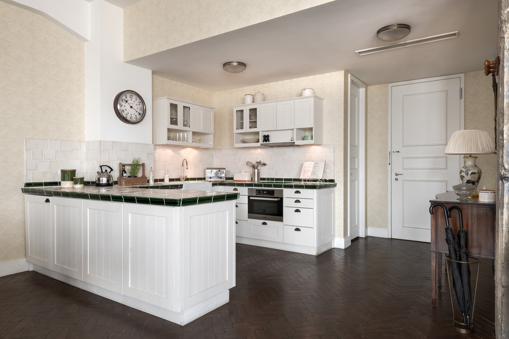 Mid-sized traditional u-shaped eat-in kitchen in Berlin with a drop-in sink, recessed-panel cabinets, white cabinets, white splashback, panelled appliances, carpet, a peninsula, brown floor and multi-coloured benchtop.