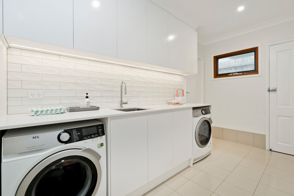 Photo of a mid-sized single-wall dedicated laundry room in Brisbane with an undermount sink, flat-panel cabinets, white cabinets, quartz benchtops, white walls, ceramic floors, a side-by-side washer and dryer, beige floor and white benchtop.