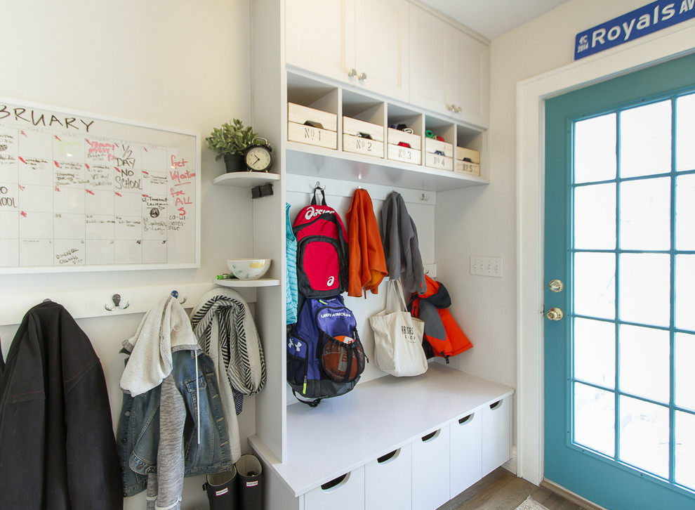 Example of a mid-sized transitional u-shaped light wood floor and brown floor mudroom design in Tampa with a farmhouse sink, recessed-panel cabinets, white cabinets, granite countertops, white backsplash, subway tile backsplash, stainless steel appliances, a peninsula, white walls and a blue front door