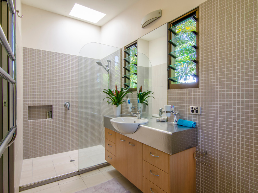 This is an example of a mid-sized tropical master bathroom in Sunshine Coast with a drop-in sink, flat-panel cabinets, light wood cabinets, stainless steel benchtops, an open shower, mosaic tile, white walls, porcelain floors, beige tile and an open shower.
