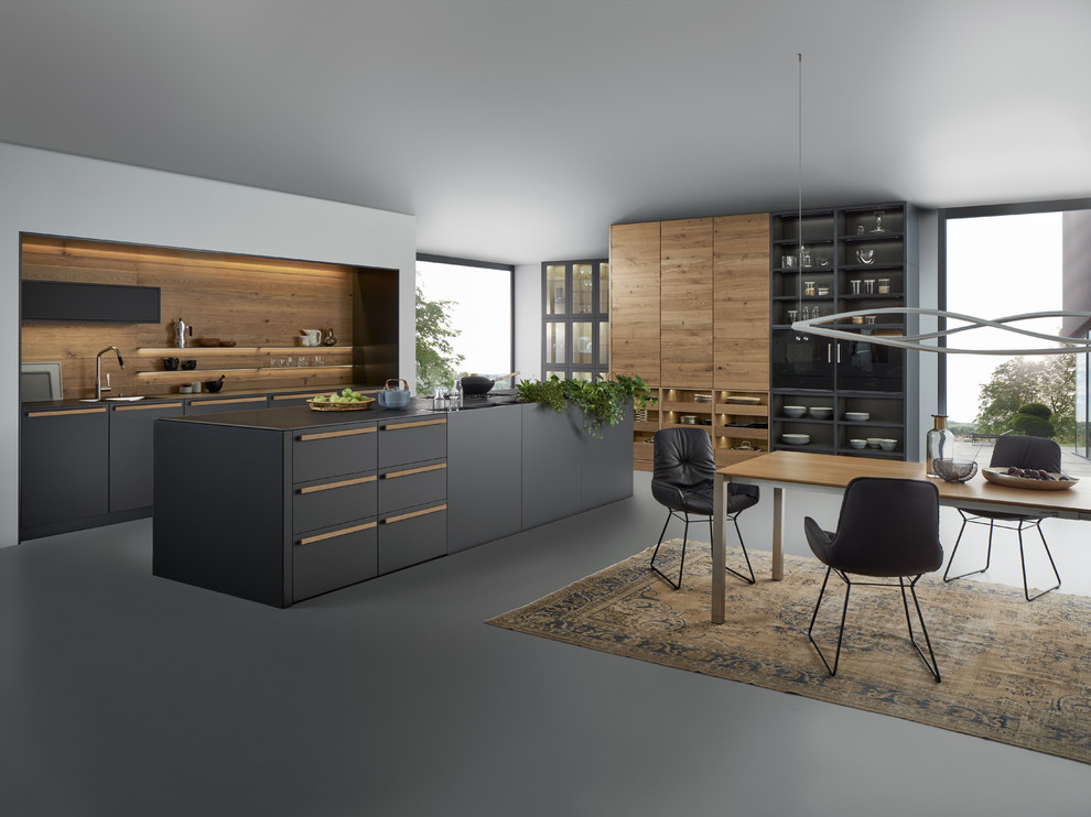 Large modern single-wall open plan kitchen in Vancouver with an integrated sink, flat-panel cabinets, black cabinets, timber splashback, black appliances, concrete floors and with island.