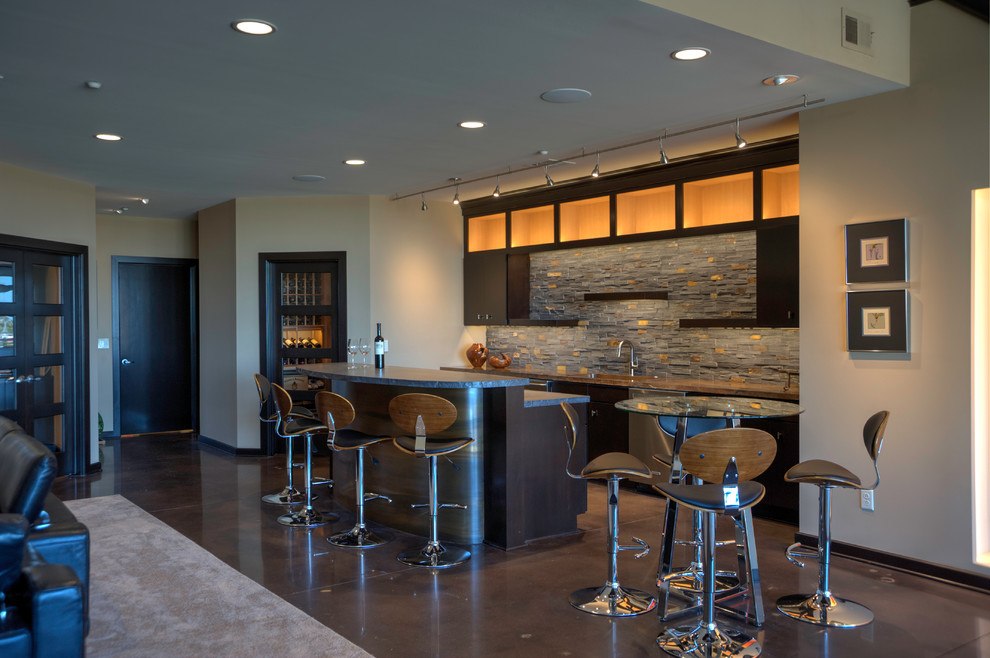 This is an example of a mid-sized modern single-wall seated home bar in Wichita with an undermount sink, shaker cabinets, dark wood cabinets, granite benchtops, grey splashback, stone tile splashback, concrete floors and brown floor.