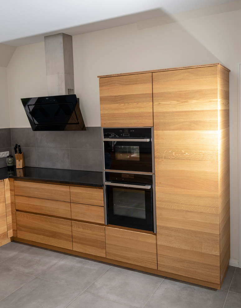 This is an example of an expansive contemporary u-shaped separate kitchen in Bremen with flat-panel cabinets, light wood cabinets, granite benchtops, panelled appliances, no island, grey floor and black benchtop.