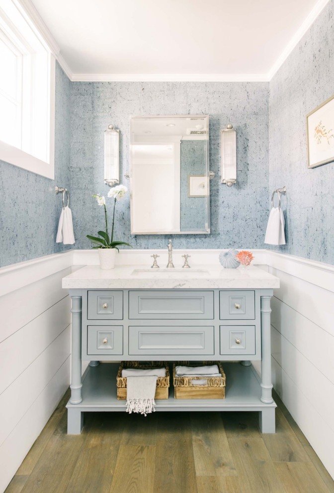 Inspiration for a beach style bathroom in Los Angeles with recessed-panel cabinets, grey cabinets, grey walls, medium hardwood floors, an undermount sink, brown floor, white benchtops, a single vanity, a freestanding vanity, decorative wall panelling and wallpaper.