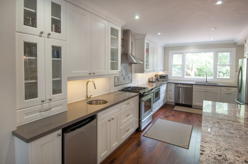 Large transitional u-shaped medium tone wood floor open concept kitchen photo in Toronto with a double-bowl sink, shaker cabinets, white cabinets, quartzite countertops, white backsplash, ceramic backsplash, stainless steel appliances and an island