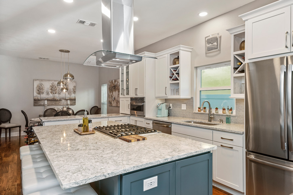 Design ideas for a large beach style l-shaped open plan kitchen in Tampa with an undermount sink, shaker cabinets, white cabinets, quartz benchtops, grey splashback, glass tile splashback, stainless steel appliances, medium hardwood floors, with island, brown floor and grey benchtop.