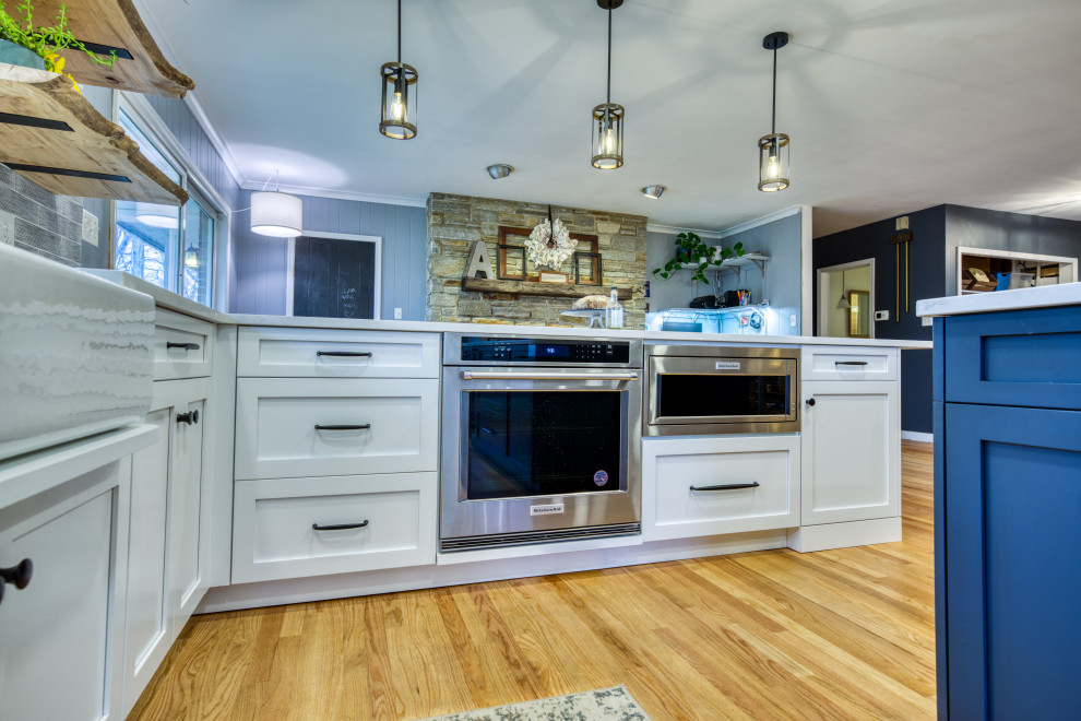 Bild på ett stort vintage vit vitt u-kök, med vita skåp, bänkskiva i kvarts, blått stänkskydd, stänkskydd i keramik, rostfria vitvaror, mellanmörkt trägolv och en köksö
