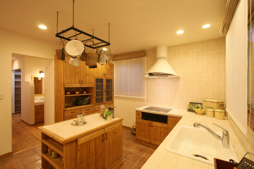 This is an example of a mediterranean l-shaped separate kitchen in Other with terra-cotta floors, brown floor, a single-bowl sink, tile benchtops and with island.
