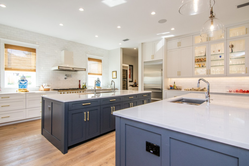 Expansive traditional galley kitchen/diner in Tampa with a submerged sink, raised-panel cabinets, white cabinets, quartz worktops, white splashback, metro tiled splashback, stainless steel appliances, medium hardwood flooring, multiple islands, brown floors and white worktops.