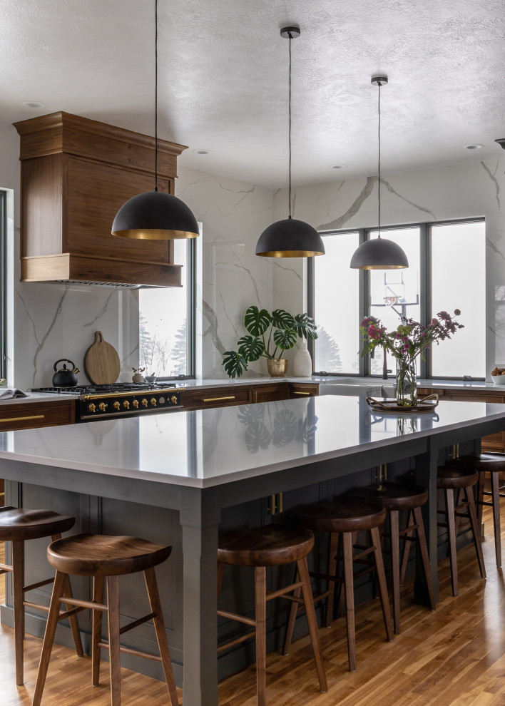 Example of a mid-sized transitional l-shaped light wood floor and brown floor eat-in kitchen design with a farmhouse sink, shaker cabinets, blue cabinets, quartz countertops, white backsplash, quartz backsplash, black appliances, an island and white countertops