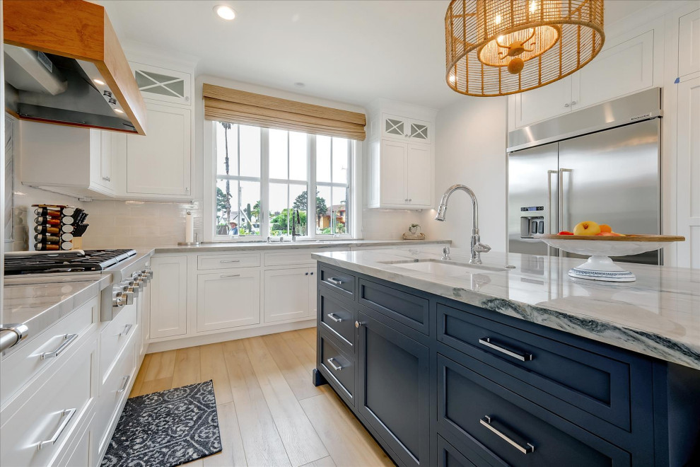 Inspiration for a mid-sized coastal l-shaped vinyl floor and beige floor eat-in kitchen remodel in San Francisco with a farmhouse sink, beaded inset cabinets, white cabinets, quartzite countertops, white backsplash, ceramic backsplash, stainless steel appliances, an island and gray countertops