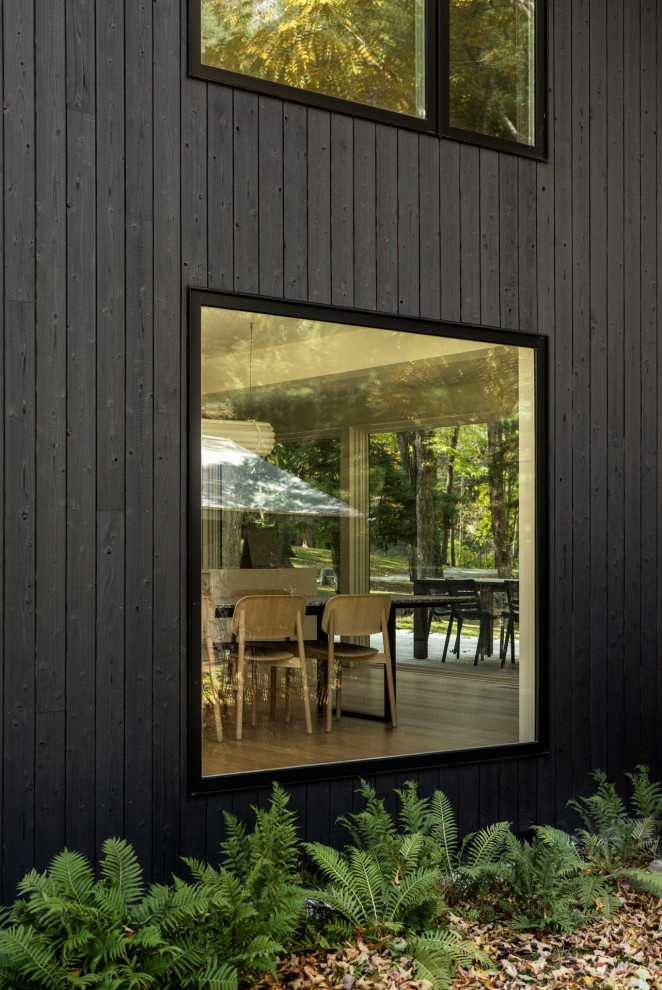 Cette image montre une façade de maison noire design en bois de taille moyenne et à un étage avec un toit en métal et un toit noir.