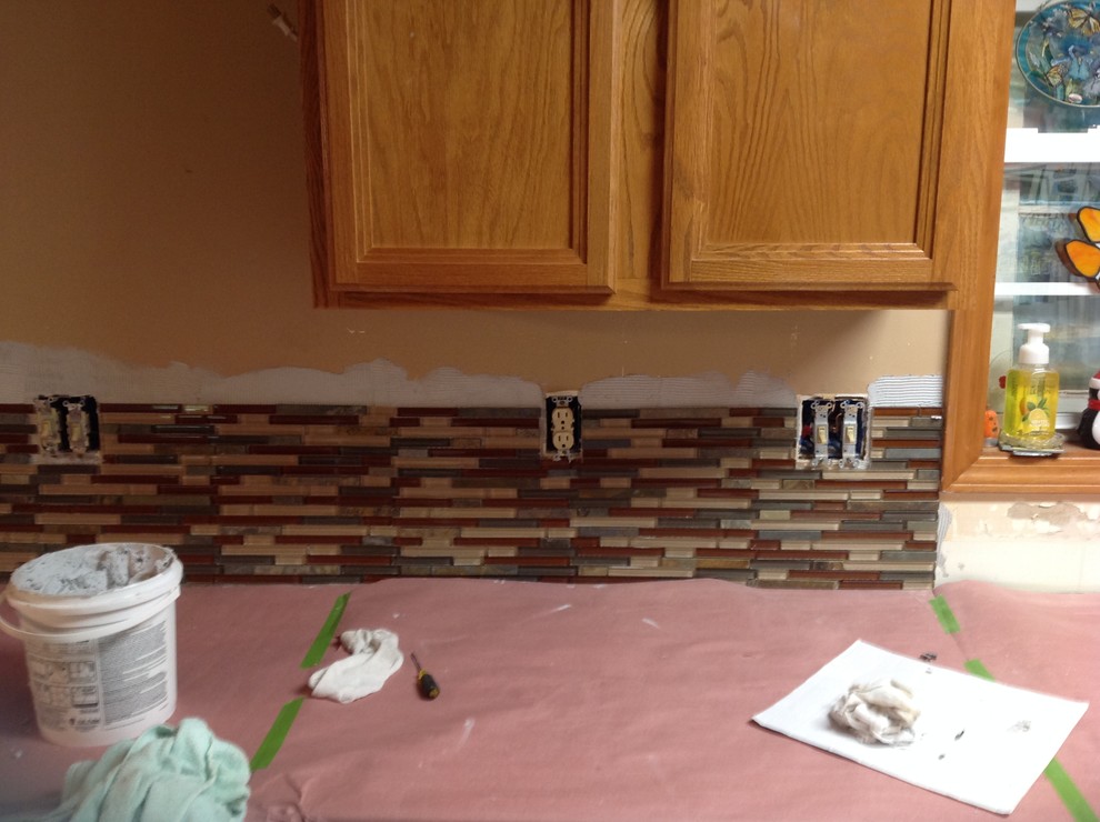 L-shaped eat-in kitchen photo with an undermount sink, flat-panel cabinets, brown backsplash, glass tile backsplash, stainless steel appliances and a peninsula