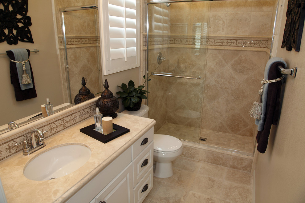 Small traditional bathroom in Orange County with raised-panel cabinets, white cabinets, a two-piece toilet, beige tile, travertine, beige walls, travertine floors, an undermount sink, beige floor, a sliding shower screen and an alcove shower.
