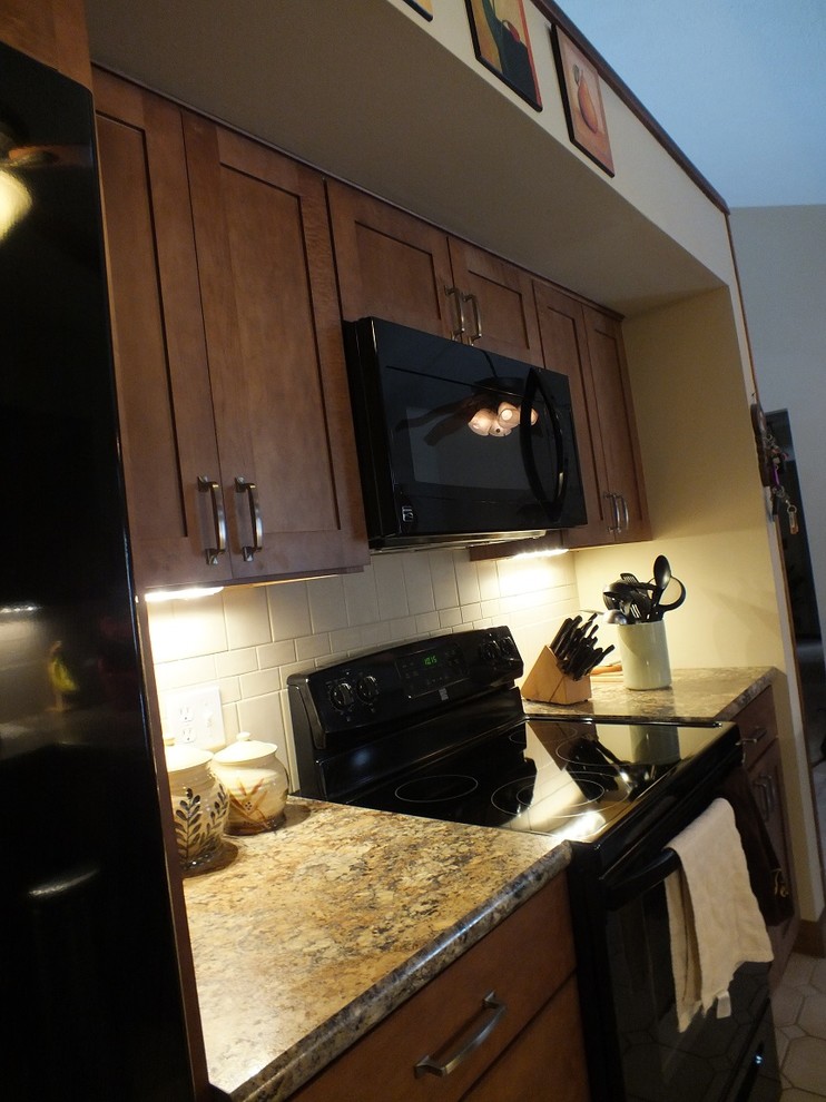 Photo of a mid-sized transitional u-shaped kitchen in Cleveland with a drop-in sink, shaker cabinets, medium wood cabinets, laminate benchtops, beige splashback, ceramic splashback, black appliances and linoleum floors.