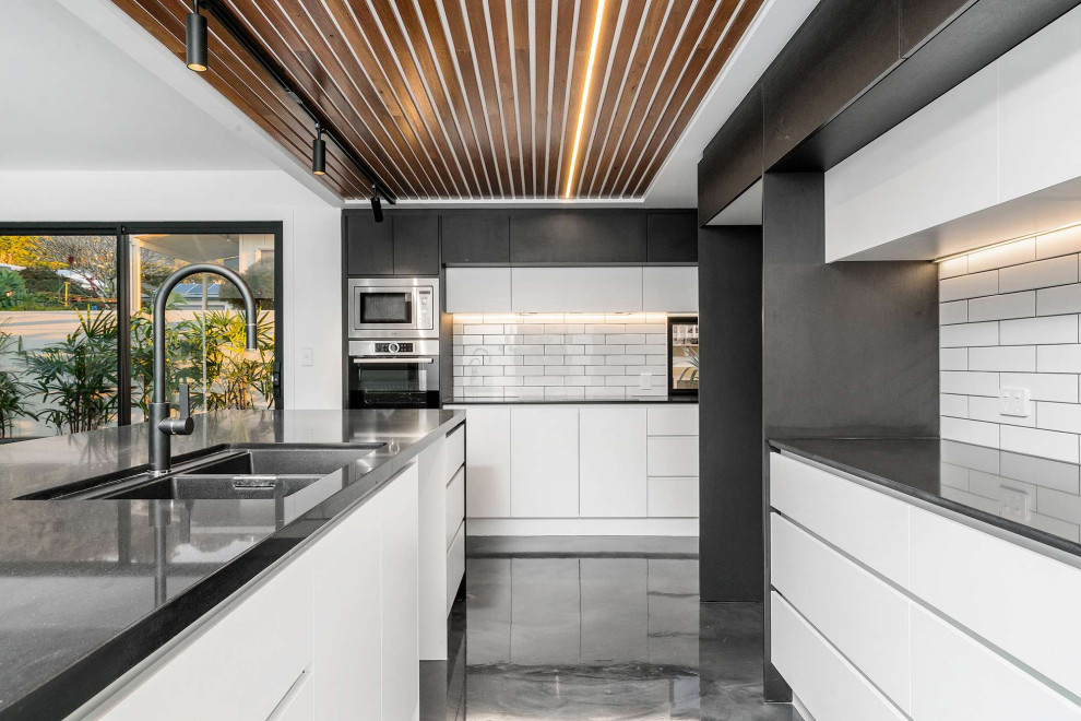 Large contemporary kitchen in Gold Coast - Tweed with an undermount sink, flat-panel cabinets, white cabinets, quartz benchtops, white splashback, subway tile splashback, stainless steel appliances, concrete floors, with island, grey floor, black benchtop and wood.