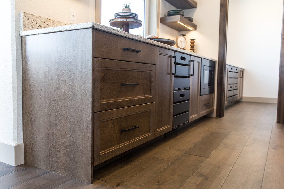 Example of a large transitional u-shaped medium tone wood floor and brown floor open concept kitchen design with a farmhouse sink, shaker cabinets, medium tone wood cabinets, quartz countertops, beige backsplash, ceramic backsplash, black appliances, an island and multicolored countertops