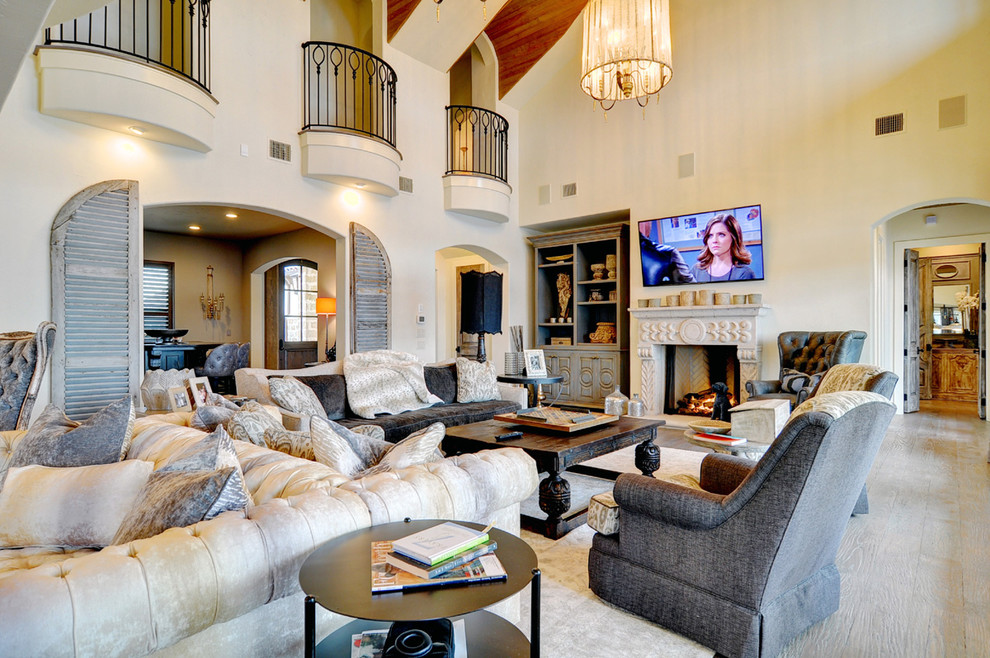 Photo of an expansive mediterranean open concept family room in Dallas with white walls, light hardwood floors, a standard fireplace, a stone fireplace surround and a wall-mounted tv.