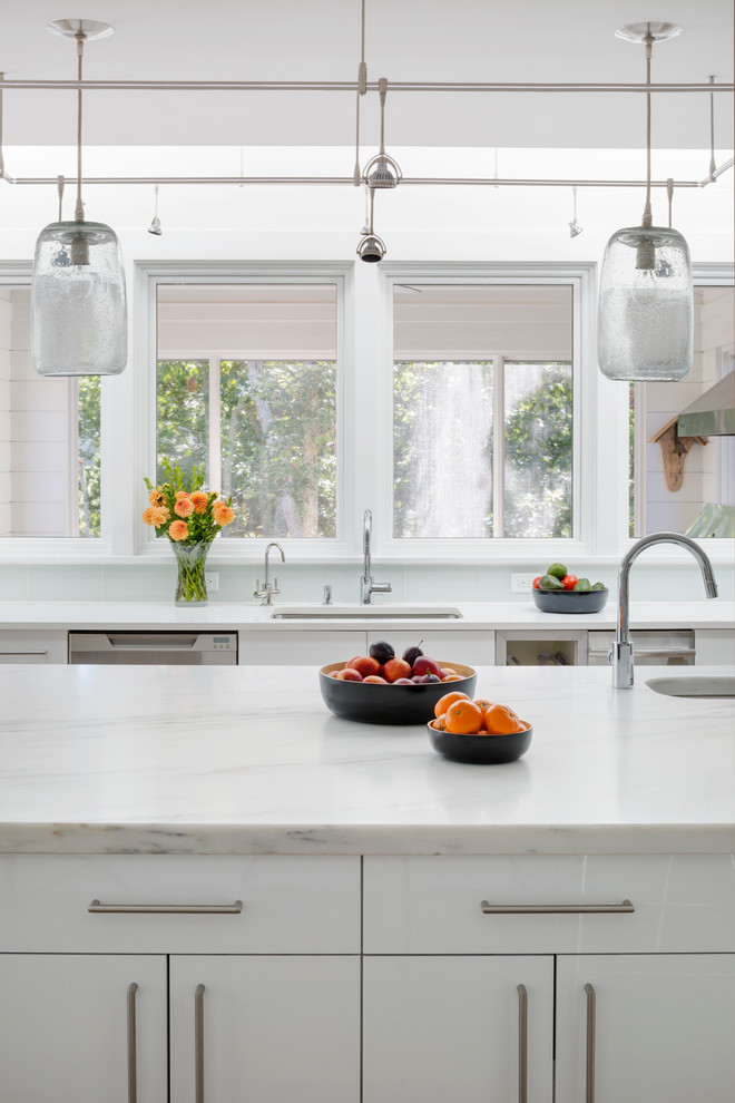 This is an example of a mid-sized beach style u-shaped eat-in kitchen in Boston with a drop-in sink, flat-panel cabinets, white cabinets, marble benchtops, blue splashback, stainless steel appliances, light hardwood floors, with island and glass tile splashback.