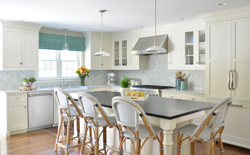 Elegant l-shaped medium tone wood floor kitchen photo in Boston with a farmhouse sink, white cabinets, stone tile backsplash, an island, shaker cabinets, white backsplash and stainless steel appliances