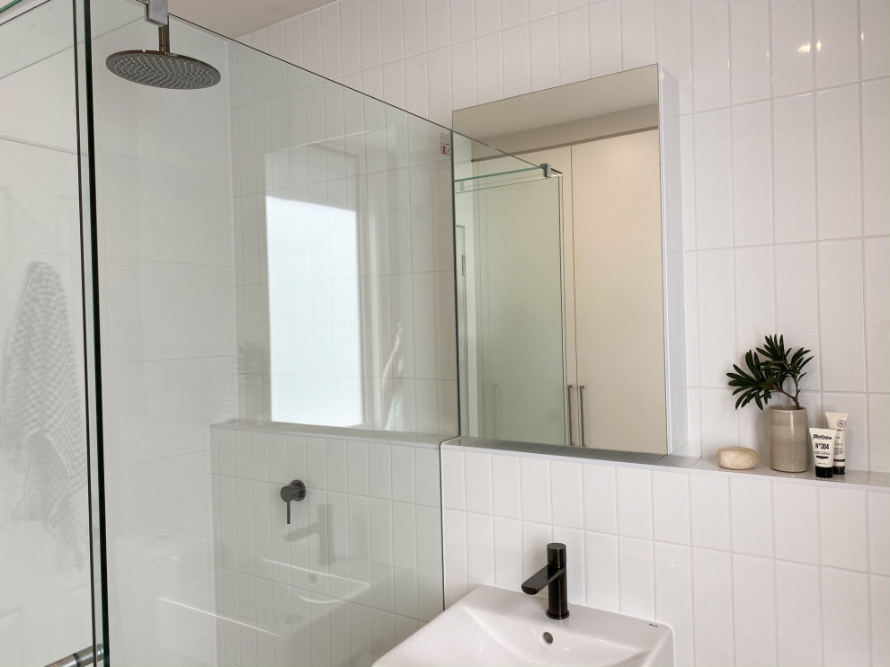 Inspiration for a small contemporary bathroom in Melbourne with a corner shower, white tile, subway tile, porcelain floors, a wall-mount sink, brown floor, a hinged shower door and a single vanity.