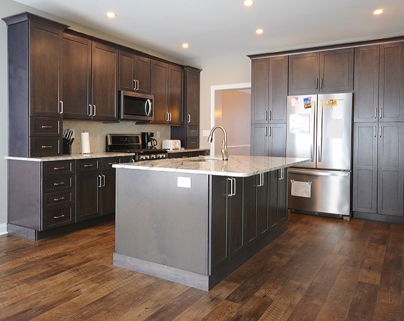 Large transitional l-shaped eat-in kitchen in Philadelphia with an undermount sink, recessed-panel cabinets, grey cabinets, granite benchtops, white splashback, subway tile splashback, stainless steel appliances, vinyl floors, with island, brown floor and multi-coloured benchtop.