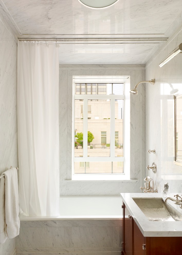 Photo of a small traditional master bathroom in New York with an undermount sink, medium wood cabinets, an alcove tub, a shower/bathtub combo, white tile, stone slab, white walls and marble benchtops.
