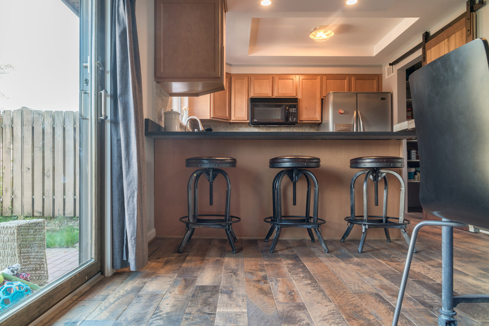 Photo of a mid-sized country u-shaped eat-in kitchen in New York with an undermount sink, brown cabinets, granite benchtops, stainless steel appliances, medium hardwood floors, shaker cabinets, grey splashback, stone tile splashback, a peninsula and multi-coloured floor.