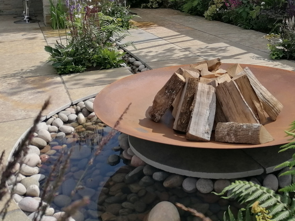 Photo of a rustic back garden in West Midlands with natural stone paving, a wood fence and a fire feature.