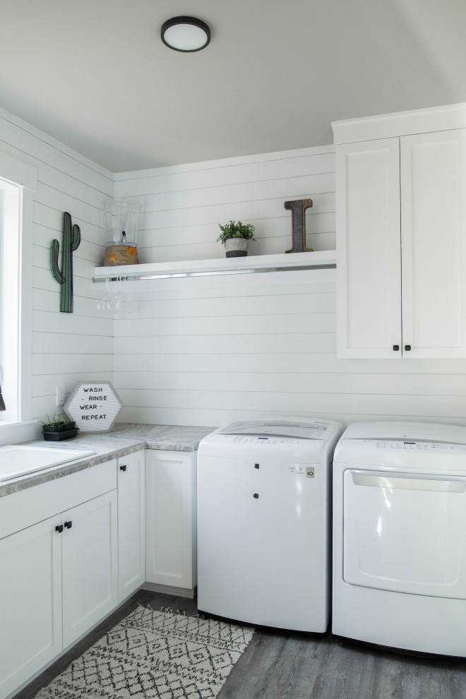 Inspiration for a mid-sized arts and crafts l-shaped dedicated laundry room in Portland with a drop-in sink, recessed-panel cabinets, white cabinets, limestone benchtops, white walls, painted wood floors, a side-by-side washer and dryer, grey floor and grey benchtop.