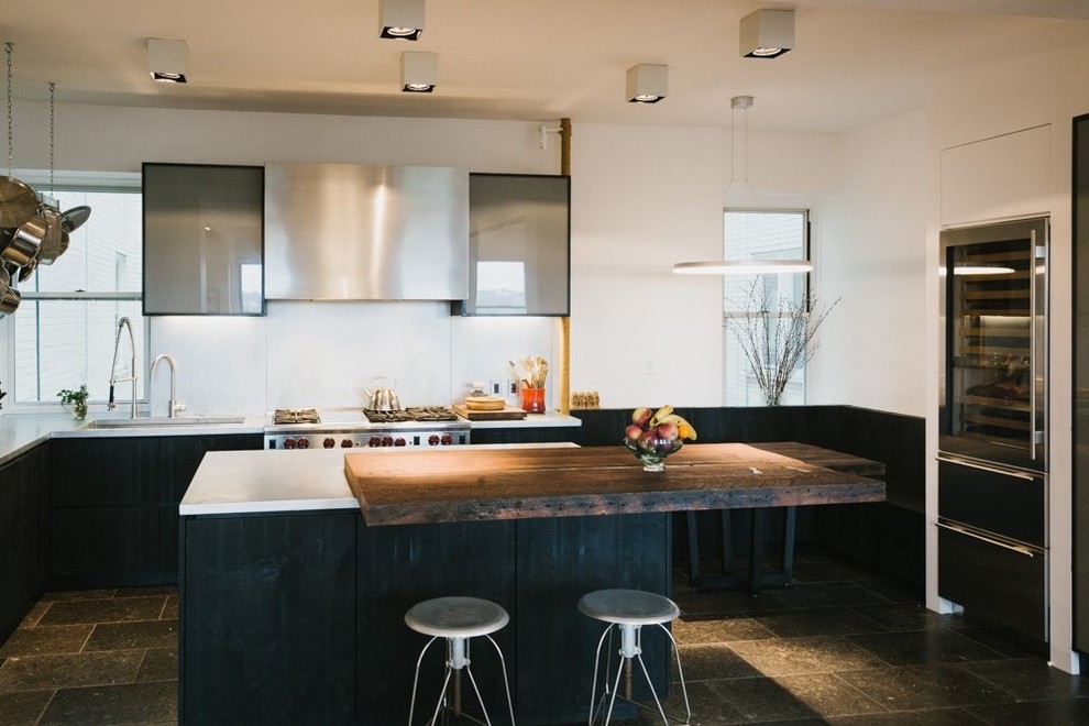 This is an example of a large contemporary u-shaped eat-in kitchen in New York with an undermount sink, flat-panel cabinets, black cabinets, solid surface benchtops, stainless steel appliances, concrete floors, with island and black floor.