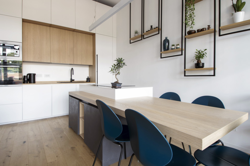 This is an example of a mid-sized contemporary open plan kitchen in Turin with an undermount sink, flat-panel cabinets, white cabinets, solid surface benchtops, white splashback, stainless steel appliances, light hardwood floors, with island, brown floor and white benchtop.