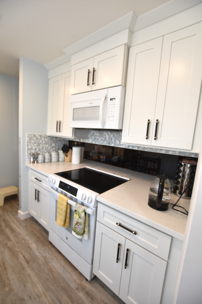 Example of a small transitional vinyl floor and brown floor enclosed kitchen design with an undermount sink, shaker cabinets, white cabinets, quartzite countertops, blue backsplash, mosaic tile backsplash, white appliances, an island and white countertops