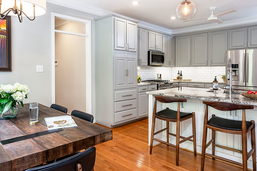 Inspiration for a mid-sized transitional l-shaped medium tone wood floor and brown floor eat-in kitchen remodel in Richmond with a farmhouse sink, gray cabinets, granite countertops, white backsplash, ceramic backsplash, stainless steel appliances, an island and multicolored countertops