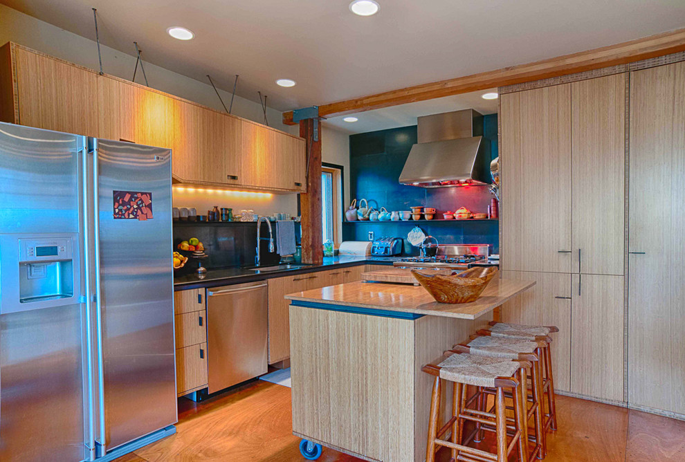 This is an example of an eclectic l-shaped kitchen in Portland with an undermount sink, flat-panel cabinets, medium wood cabinets, black splashback and stainless steel appliances.