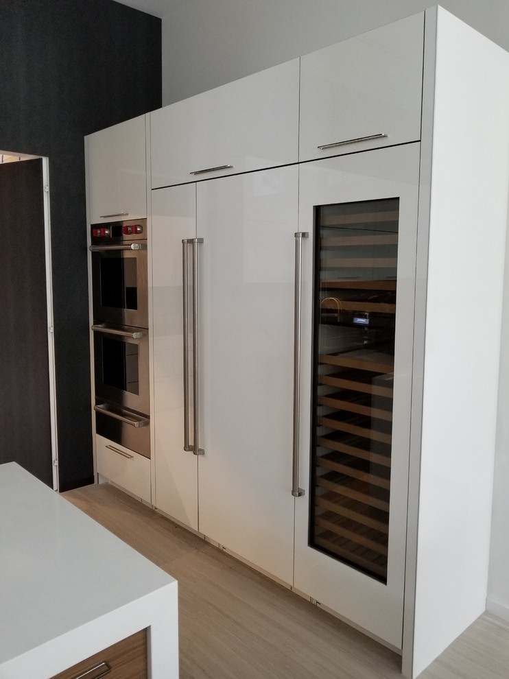 Large modern u-shaped eat-in kitchen in Miami with a drop-in sink, flat-panel cabinets, white cabinets, quartz benchtops, black splashback, stainless steel appliances, multiple islands, white benchtop and engineered quartz splashback.