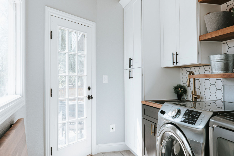 Small contemporary single-wall dedicated laundry room in Denver with a drop-in sink, shaker cabinets, white cabinets, wood benchtops, white splashback, subway tile splashback, grey walls, porcelain floors, a side-by-side washer and dryer, grey floor and brown benchtop.