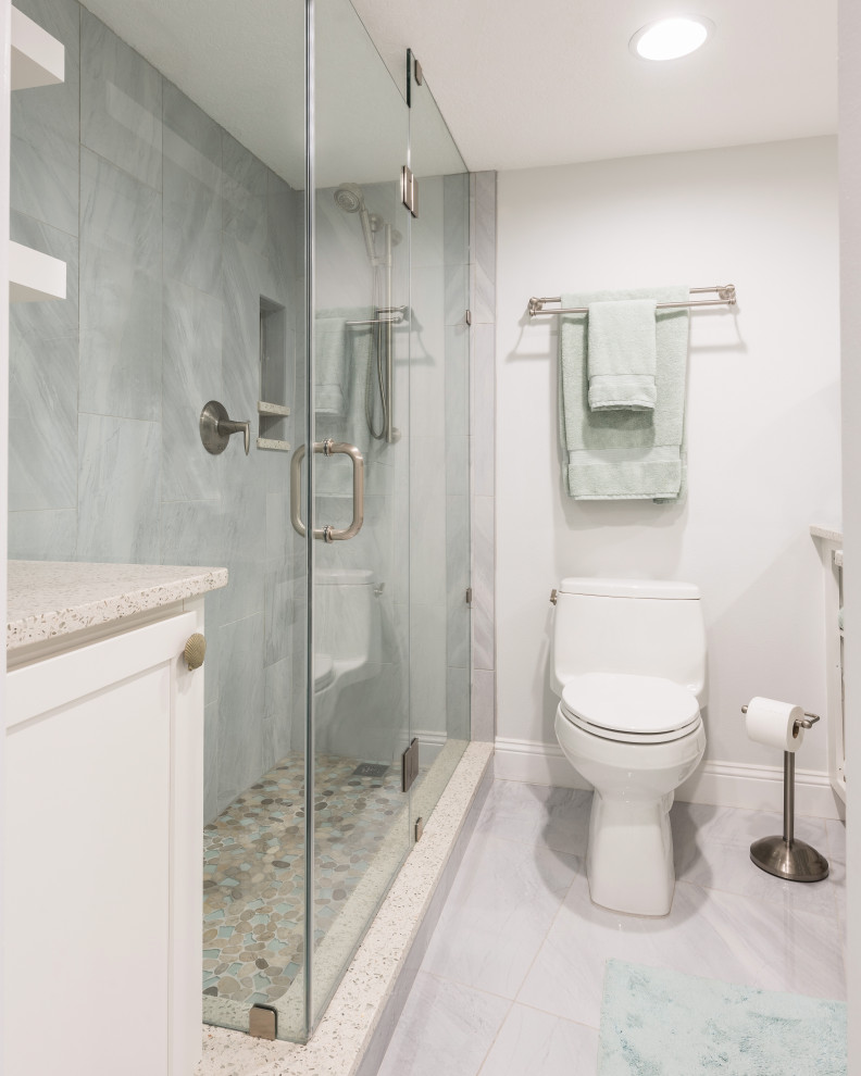 This is an example of a mid-sized beach style 3/4 bathroom in Orlando with recessed-panel cabinets, white cabinets, a corner shower, gray tile, porcelain tile, grey walls, porcelain floors, an undermount sink, recycled glass benchtops, grey floor, a hinged shower door and white benchtops.