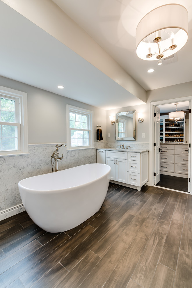 Photo of a large transitional master bathroom in Other with shaker cabinets, white cabinets, a freestanding tub, an open shower, a two-piece toilet, marble, grey walls, porcelain floors, an undermount sink, marble benchtops, brown floor and a hinged shower door.