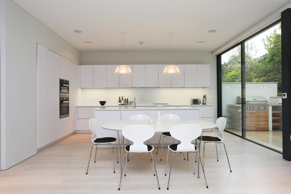 This is an example of a contemporary open plan kitchen in London with flat-panel cabinets, white cabinets, solid surface benchtops, with island and light hardwood floors.